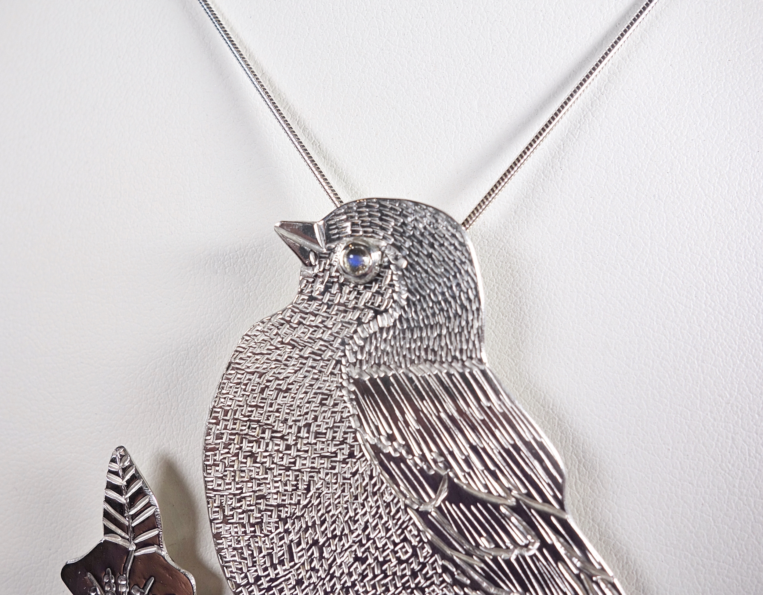 Pendentif oiseau Madame M en argent massif et péristérite, détails du ciselage et du sertis clos, vue sur fond blanc à la lumière artificielle