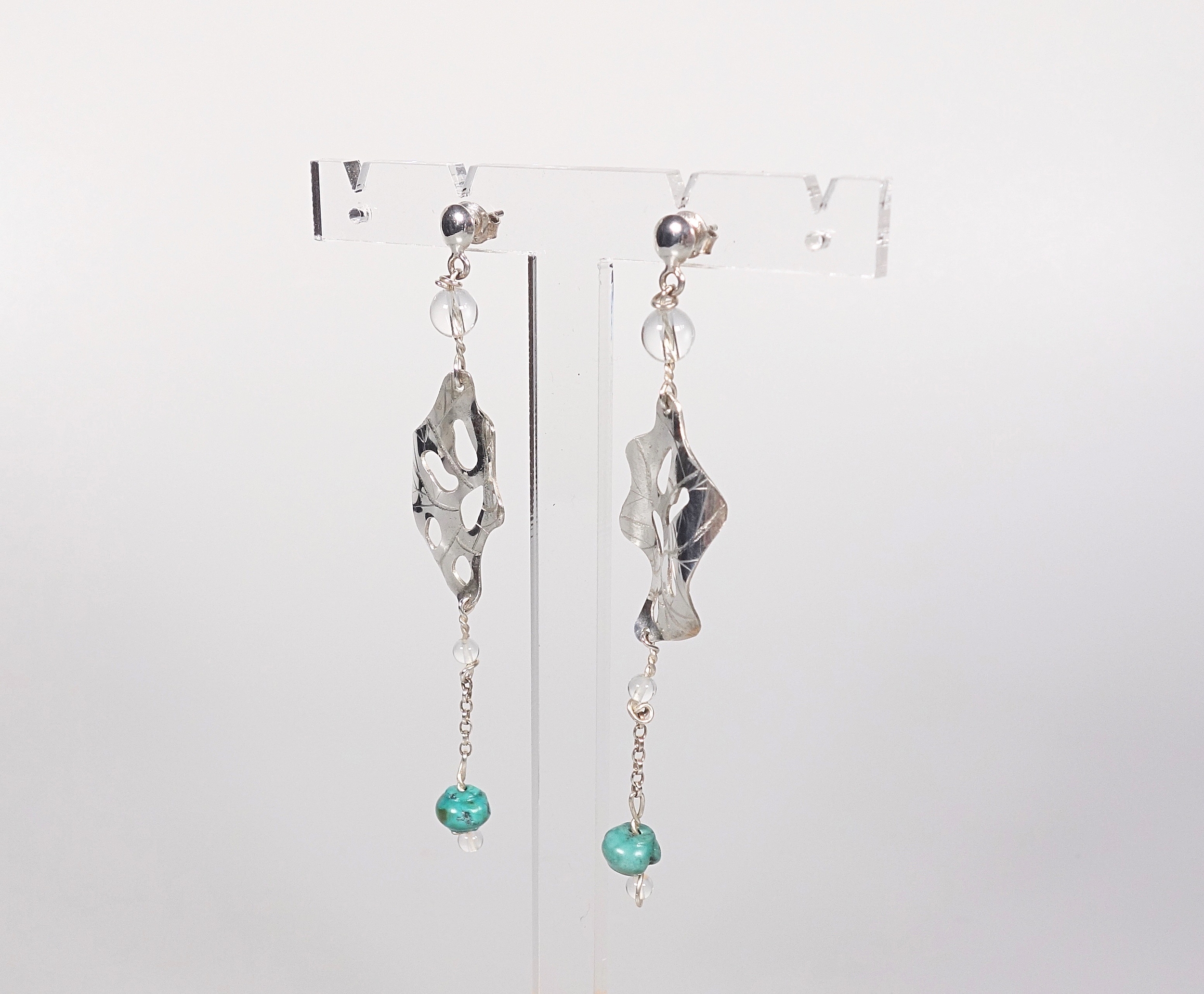 Boucles doreilles pendantes &quot;Cheyennes&quot; en argent massif et perles en turquoise et cristal de roche, vue de profil, sur présentoir et fond blanc à la lumière artificielle