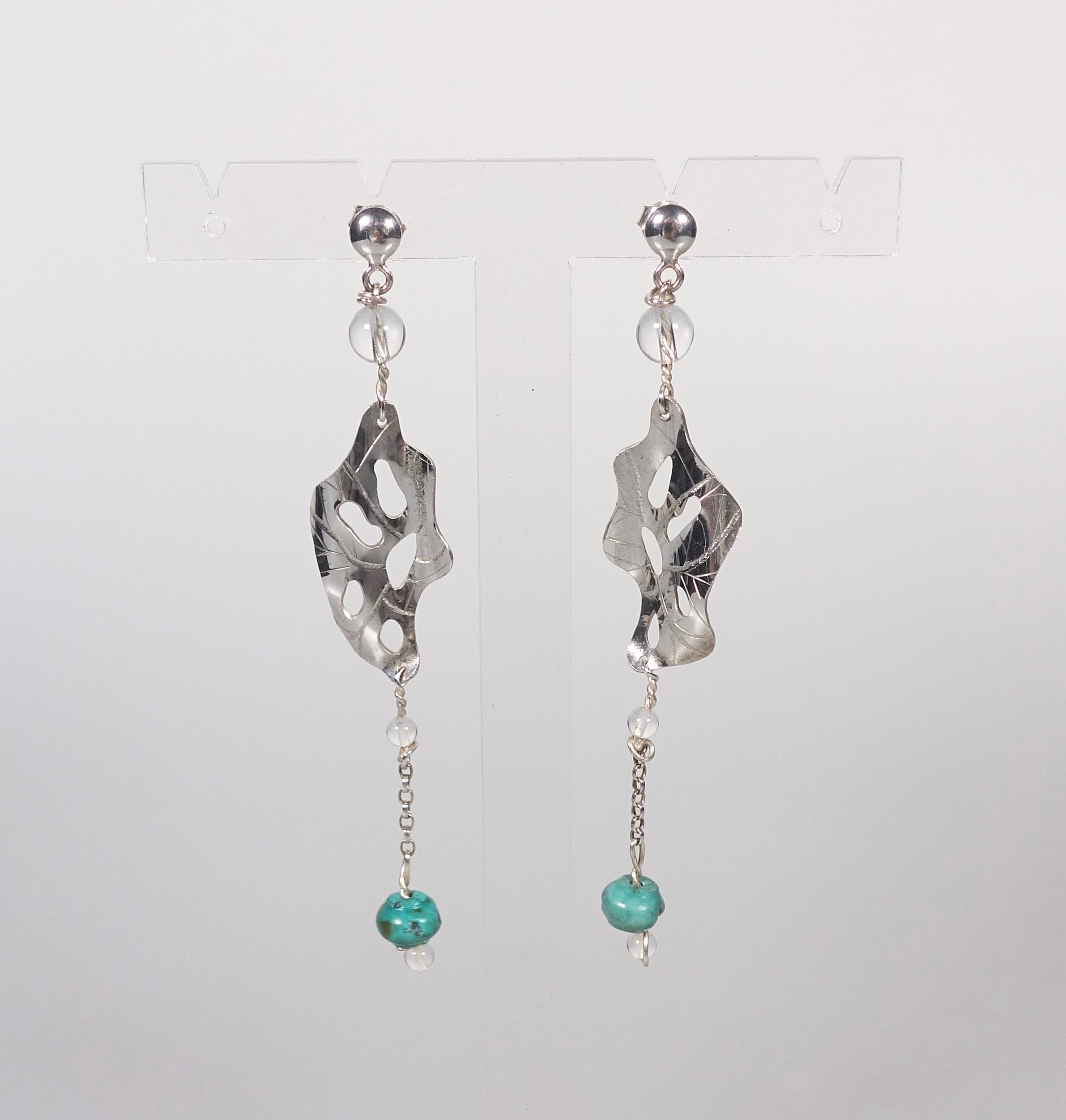 Boucles d'oreilles pendantes &quot;Cheyennes&quot; en argent massif et perles en turquoise et cristal de roche, vue de face sur présentoir et fond blanc à la lumière artificielle