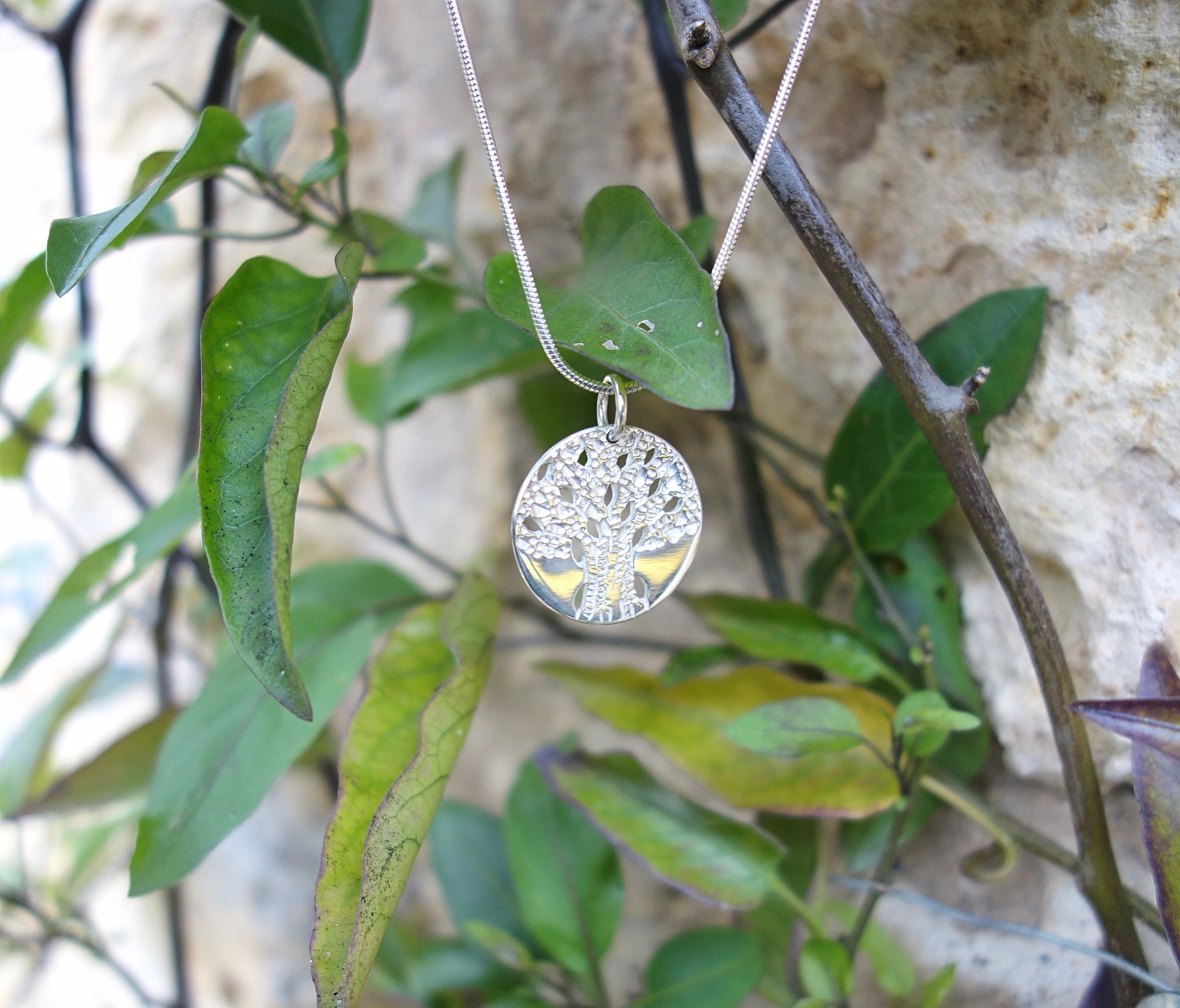 Pendentif arbre de vie en argent massif ciselé, vue de biais, en extérieur, à la lumière du jour. Création Pétale dargent.