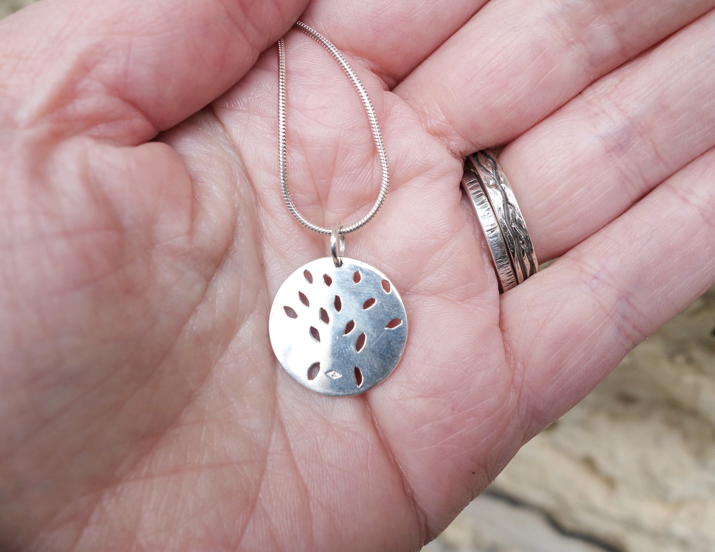 Pendentif arbre de vie en argent massif ciselé, vue de larrière, sur la main à la lumière du jour. Création Pétale dargent.