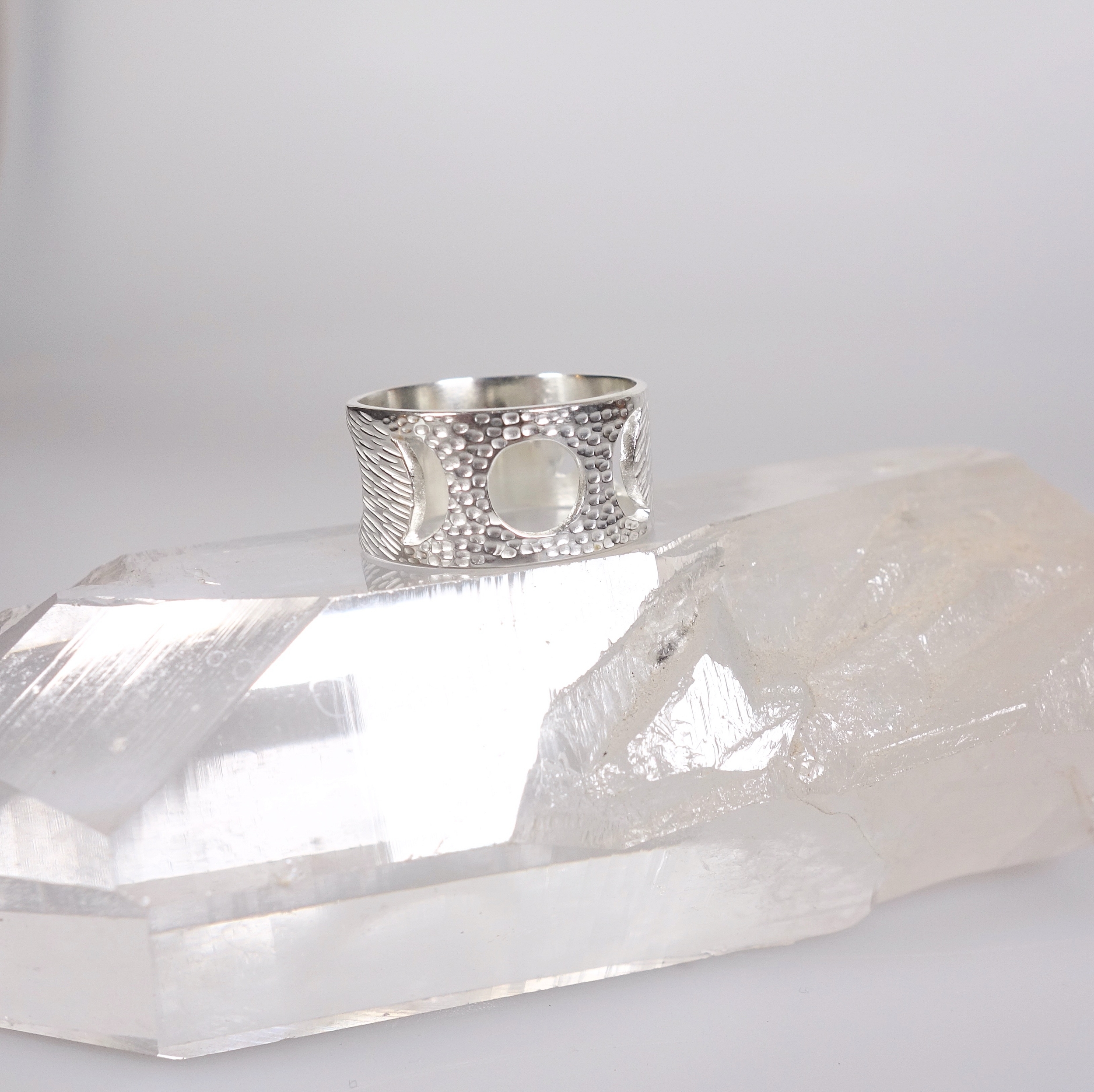 Bague féminin sacré (cycle lunaire) en argent massif ciselé, vue de profil sur un cristal de roche et un fond blanc à la lumière électrique