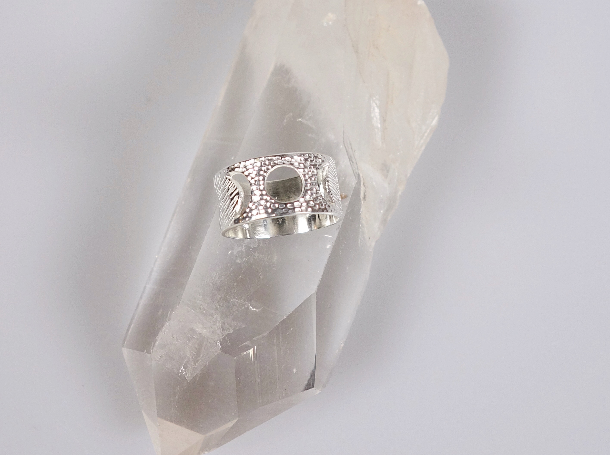 Bague féminin sacré (cycle lunaire) en argent massif ciselé, vue du dessus sur un cristal de roche et un fond blanc à la lumière électrique
