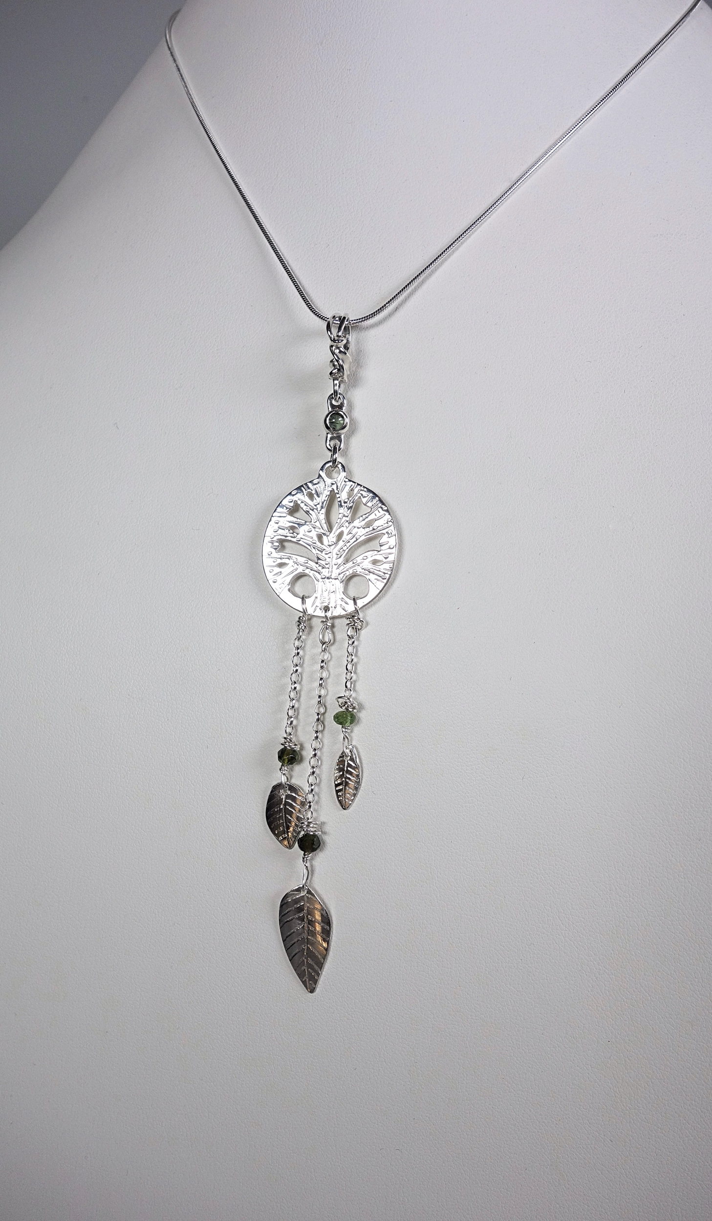 Pendentif &quot;arbre de vie&quot; avec pendants en argent massif et tourmaline verte. Talisman., vue de biais sur buste blanc et fond blanc à la lumière artificielle