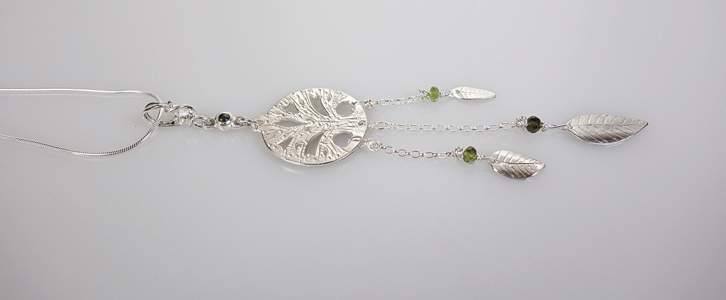 Pendentif &quot;arbre de vie&quot; avec pendants en argent massif et tourmaline verte. Talisman. Vue de profil sur fond blanc à la lumière électrique