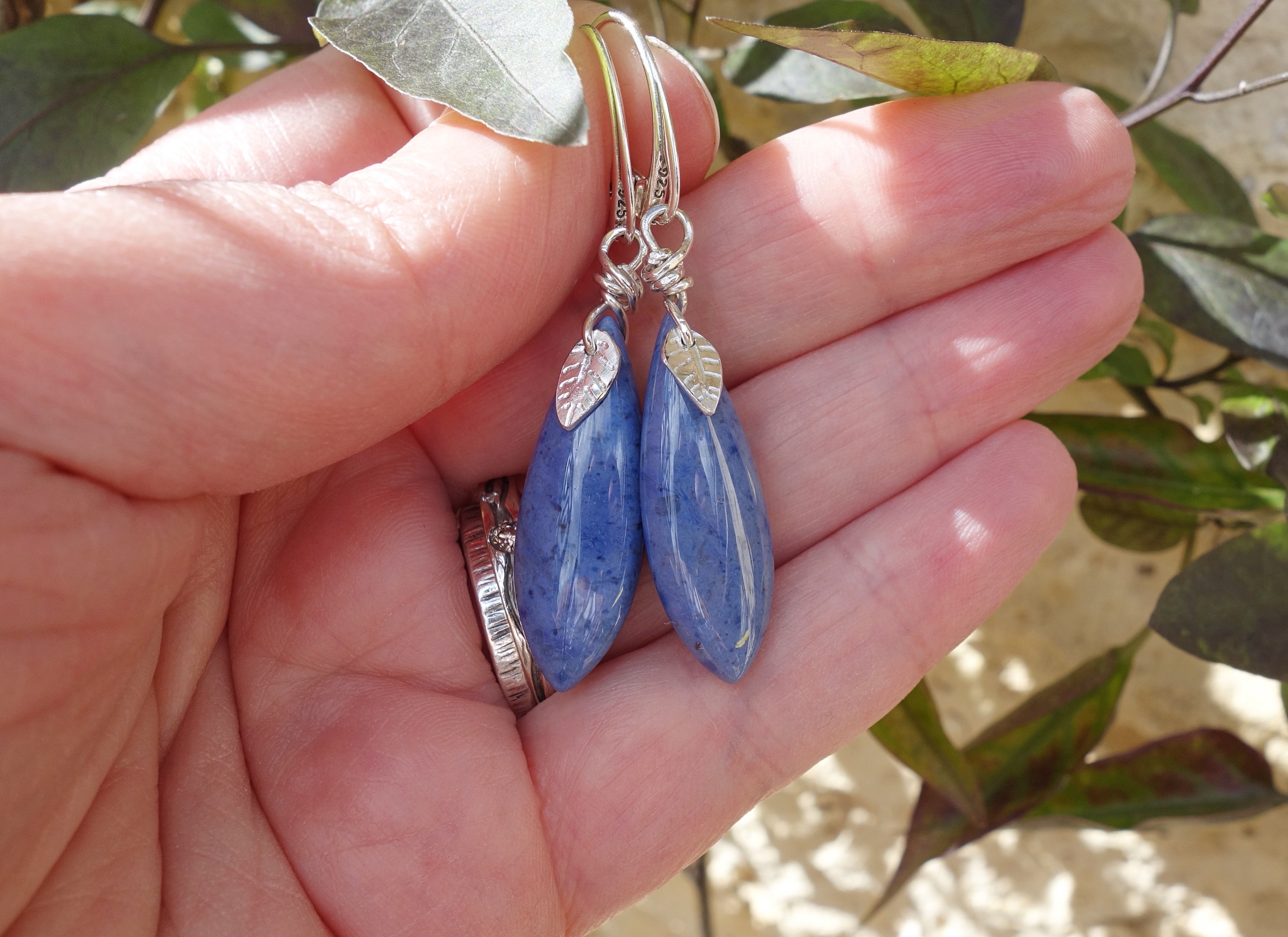 Paire de boucles doreilles en dumortiérite avec feuilles gravées et montage argent. Vue sur la main à la lumière du jour.