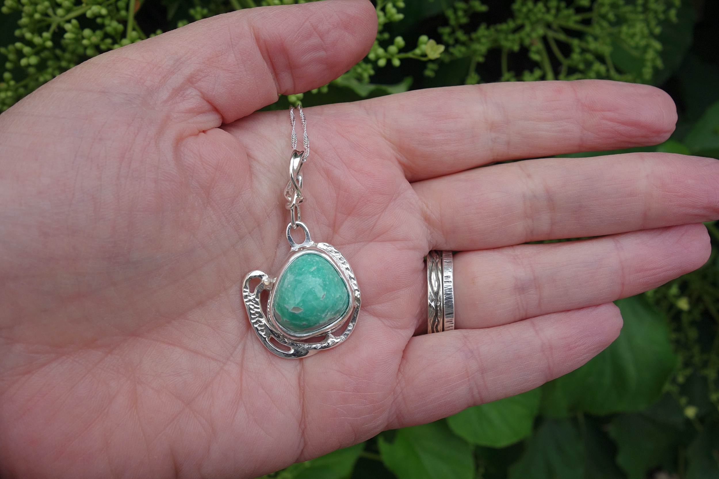Pendentif en argent massif et turquoise vu sur la main en extérieur. Pétale dargent