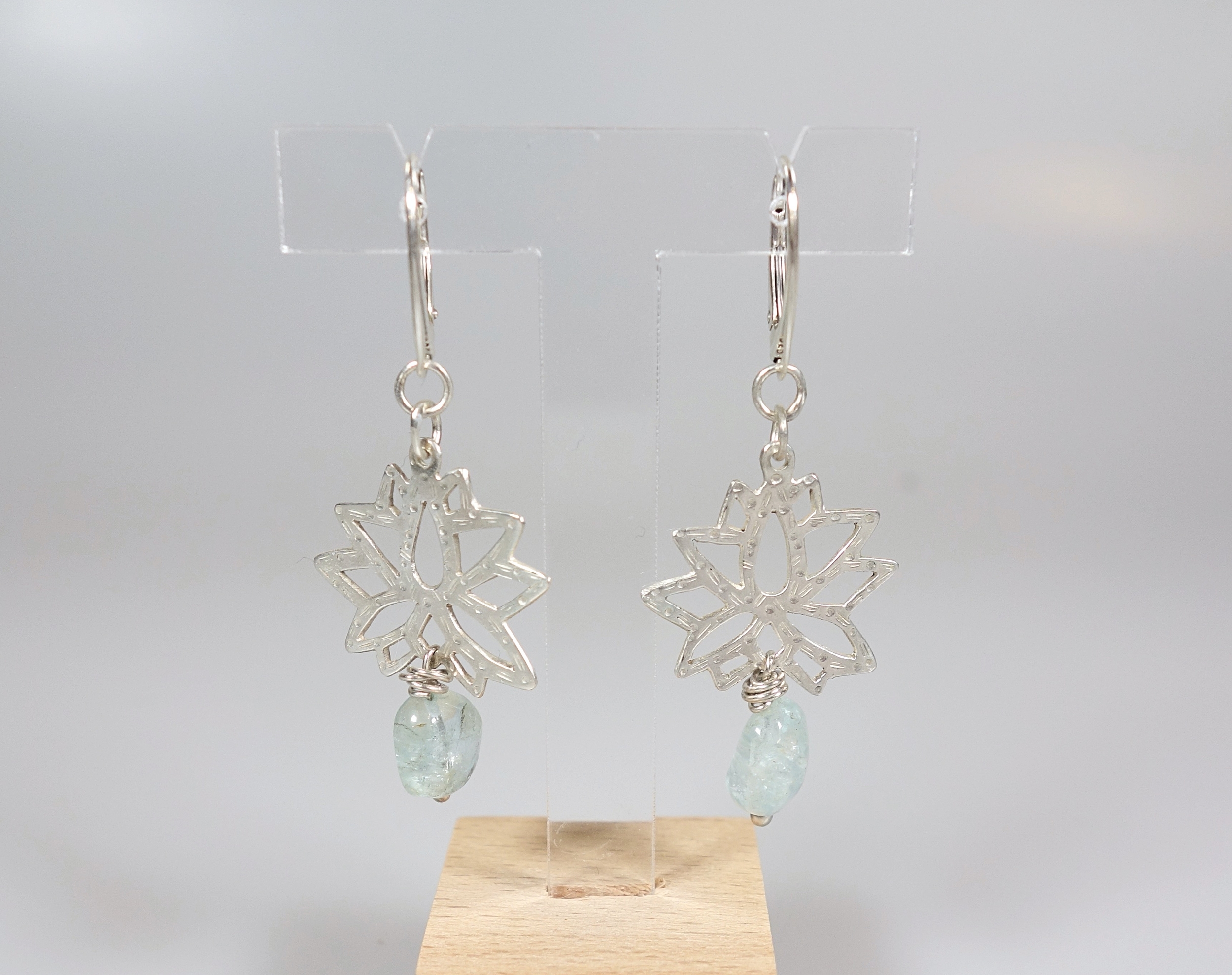 Lotus sacré. Boucles doreilles. Bijou nature. Argent et béryl. Bleu ciel. Vue de face sur fond blanc.Pétale dargent. .