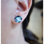 Paire de puces d'oreilles "Floral" avec émail bleu très foncé presque noir et blanc, vue portée à la lumière du jour