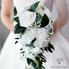 Bouquet de mariée artificiel en cascade avec des roses blanches et des touches de gypsophile, tenu par une mariée en robe blanche