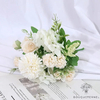 Bouquet de fleurs pour mariée composé de roses blanches, de chrysanthèmes blancs et de petites fleurs vertes, sur un fond de tissu blanc