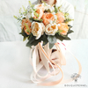 Bouquet mariée moderne avec des fleurs artificielles en tons de pêche et crème, accentué par des rubans satinés