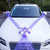 Couronne de fleurs violettes et blanches avec rubans violets, placée sur une voiture blanche pour une célébration de mariage