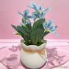 Coupe de fleurs artificielles pour cimetière bleue, avec des fleurs bleu clair épanouies dans un pot blanc décoratif
