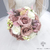 Bouquet de mariée rond aux tons pastel, composé de roses mauves, de fleurs blanches et de touches de verdure