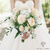 Bouquet de fleurs pour mariée élégant tenu par une mariée en robe blanche, avec des roses crème, des pivoines blanches et des touches de verdure