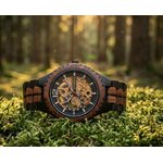 Montre automatique en bois rouge et noir, cadran squelette doré, posée sur la mousse en forêt