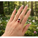 Bague à deux pierres de naissance, saphir bleu et rubis rouge en zirconium, portée à la main dans une clairière