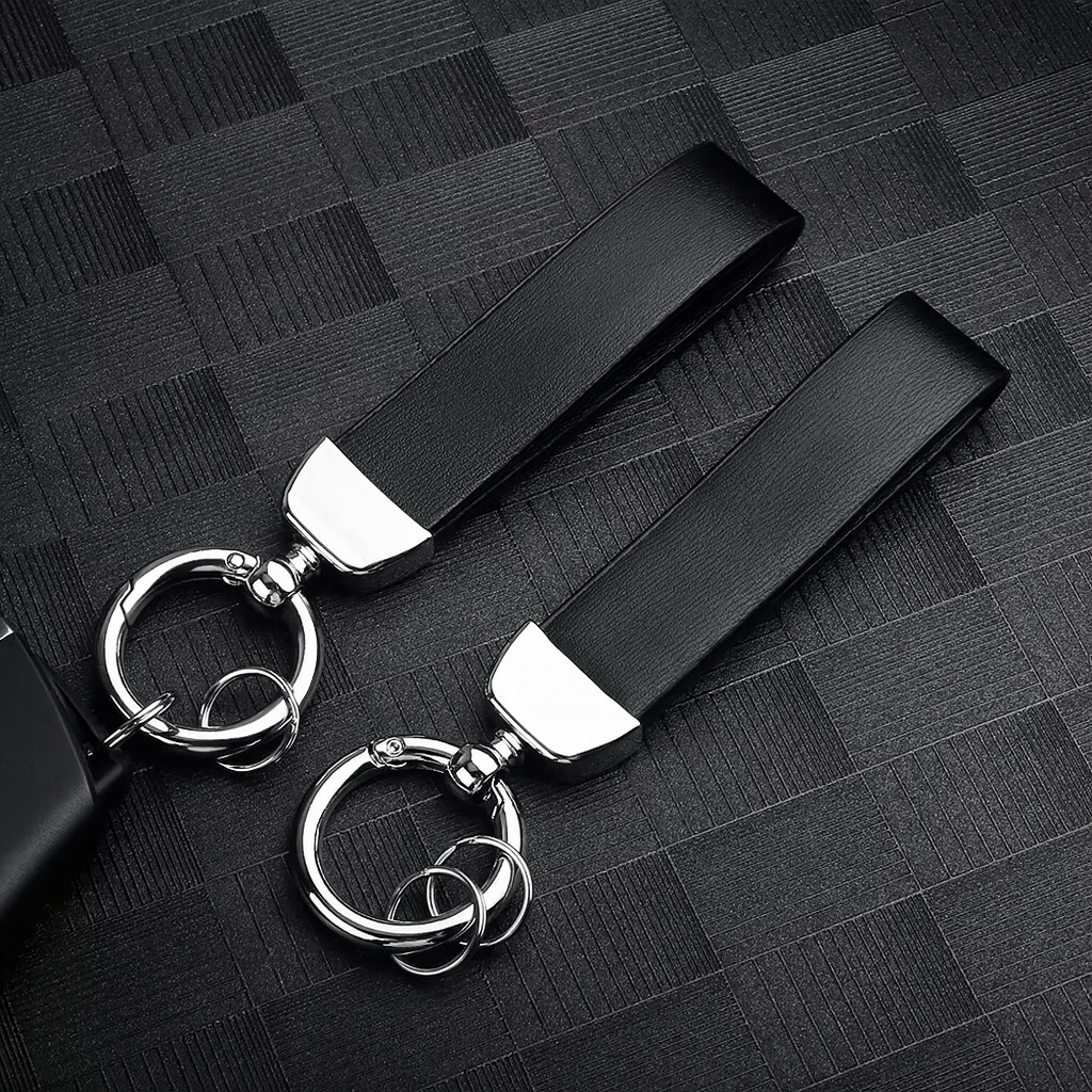 Deux porte-clés en cuir noir avec attache métallique argentée, posés sur une surface texturée noire.