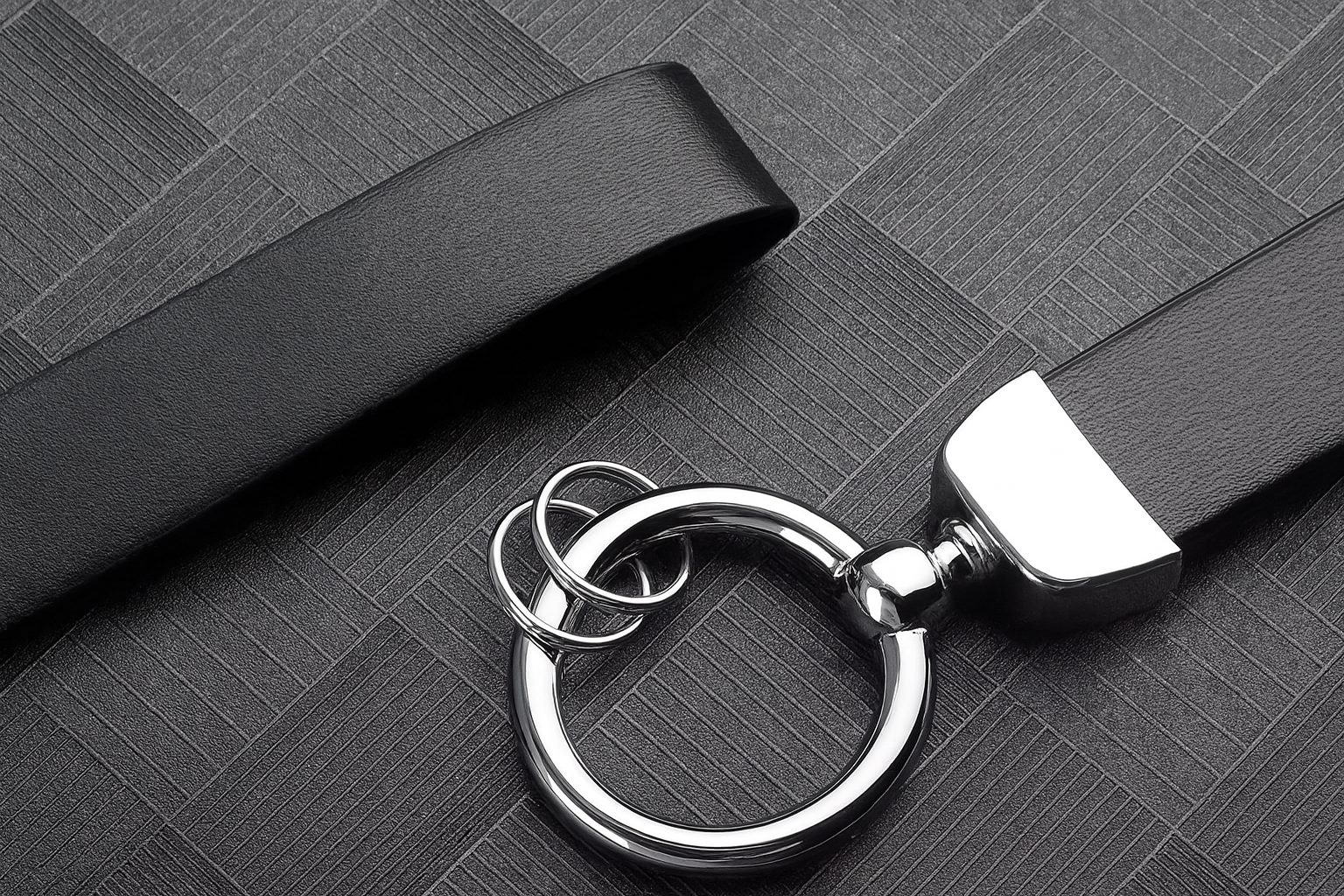 Gros plan sur un porte-clés en cuir noir, doté d’un anneau métallique argenté posé sur une surface texturée sombre