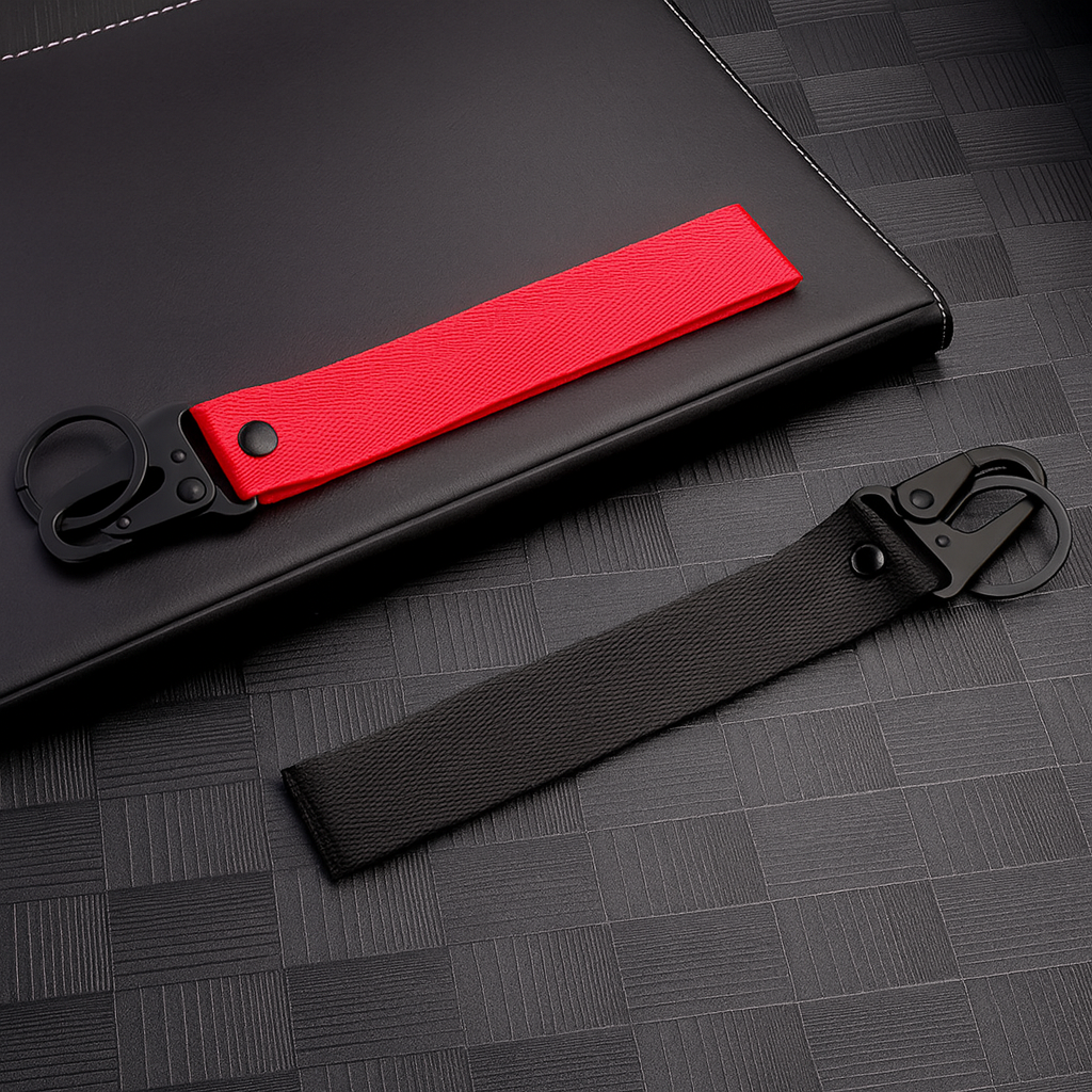 Deux porte-clés en tissu noir et rouge avec mousqueton, sans logo, posés sur fond sombre