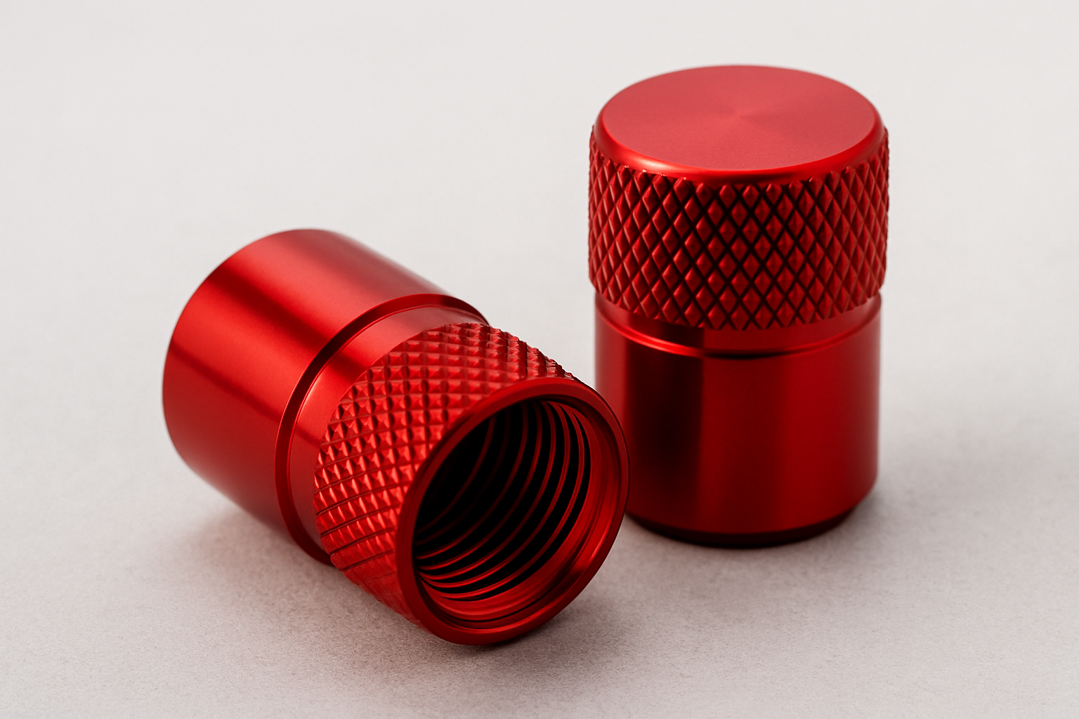Deux bouchons de valve en aluminium rouge posés sur une surface claire.