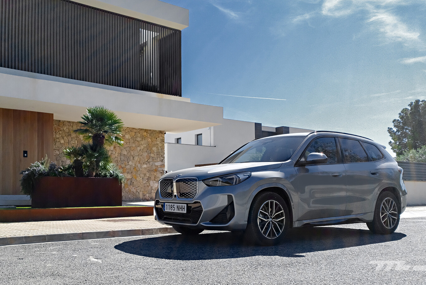 BMW iX1 gris devant une maison moderne en bord de route