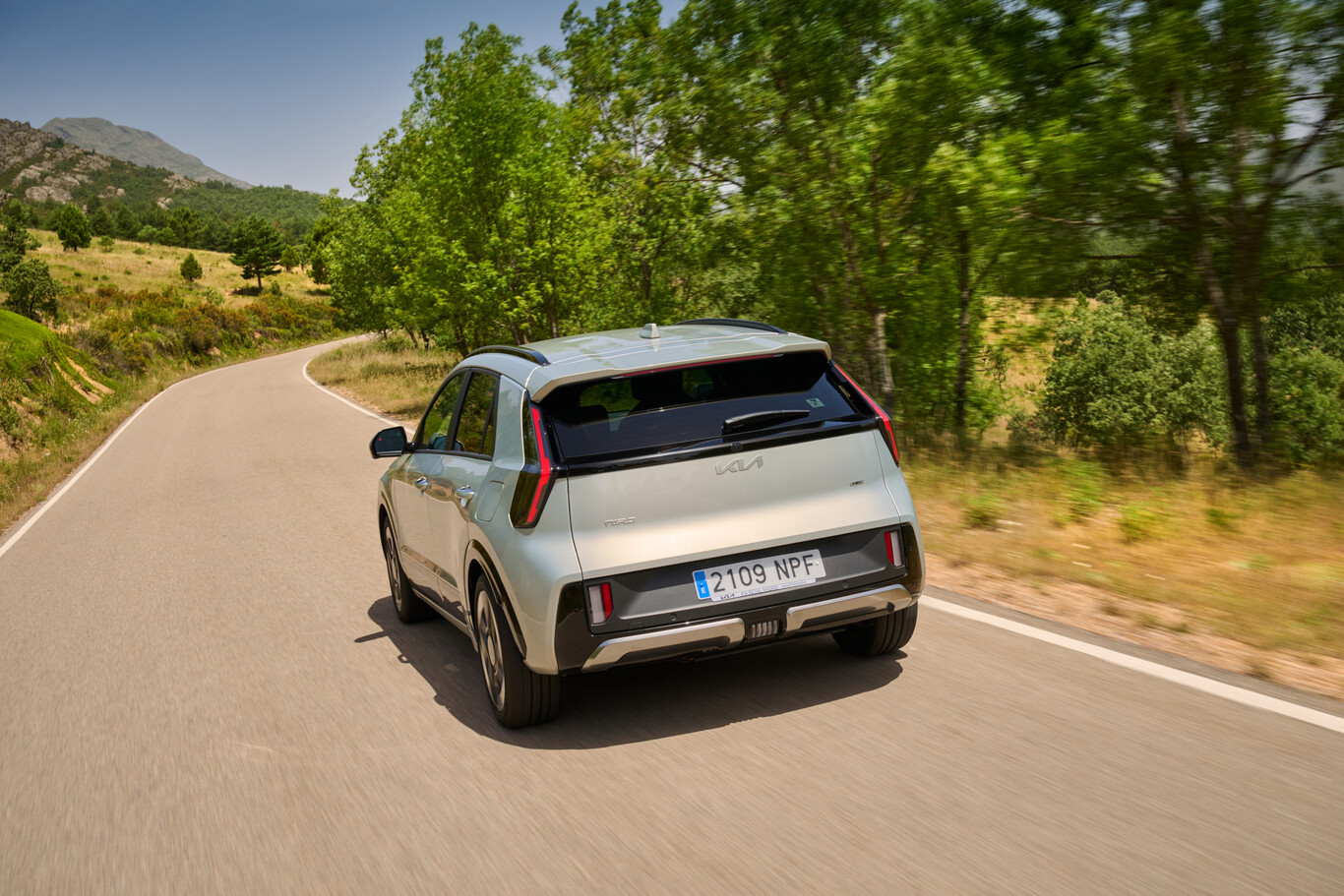Kia Niro hybride blanc vue arrière en mouvement sur une route bordée d’arbres