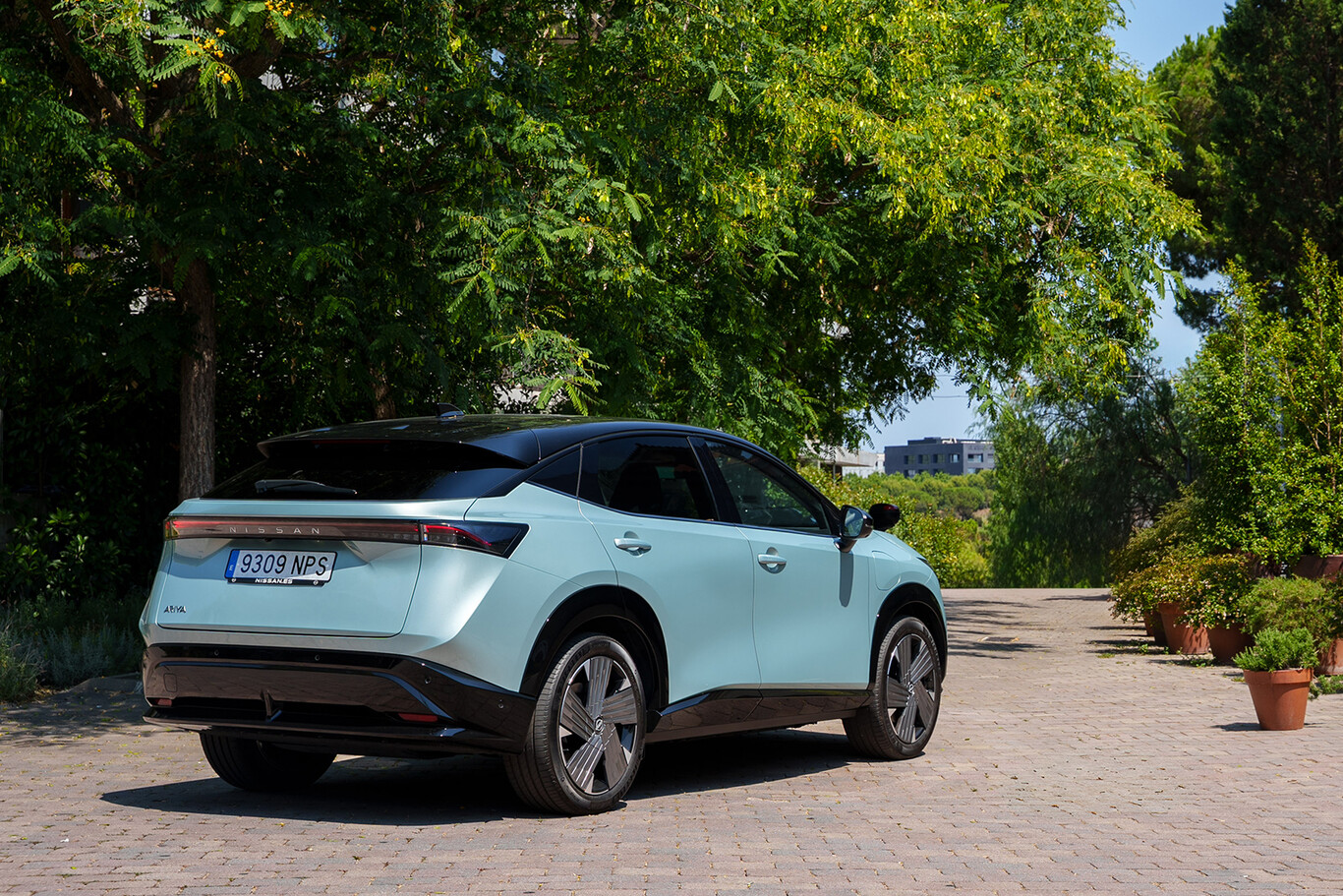 Vue arrière du Nissan Ariya électrique bleu clair stationné dans un environnement arboré