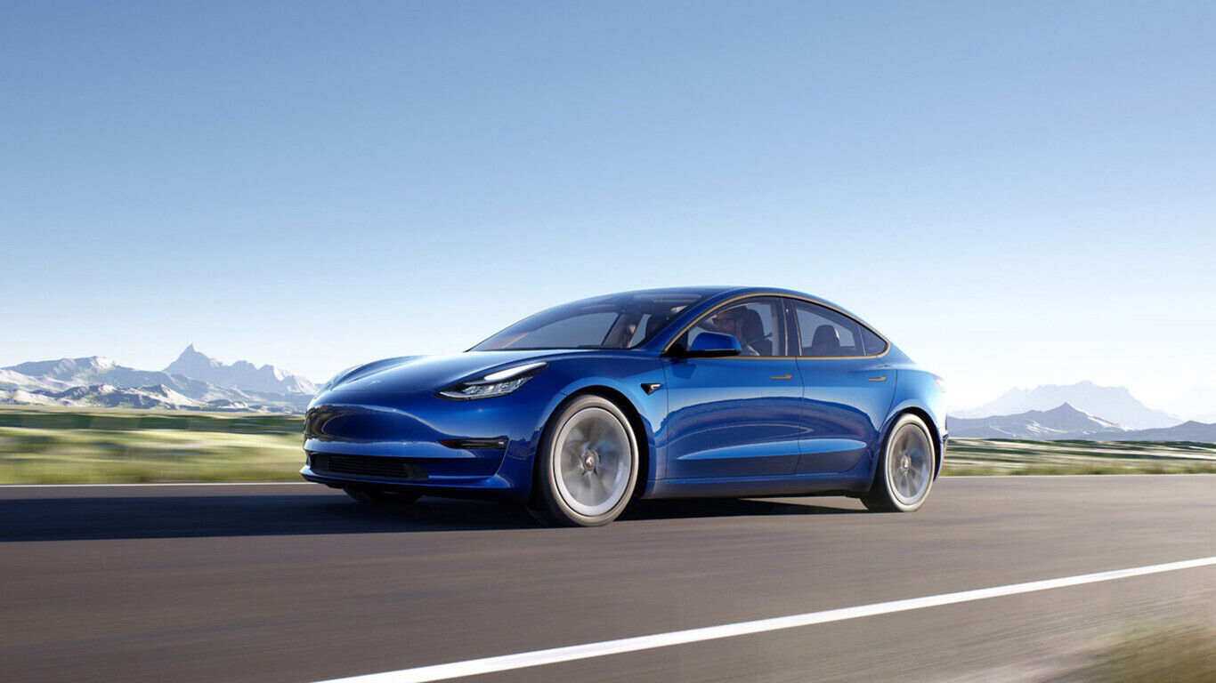 Tesla Model 3 bleue roulant sur une route avec des montagnes en arrière-plan