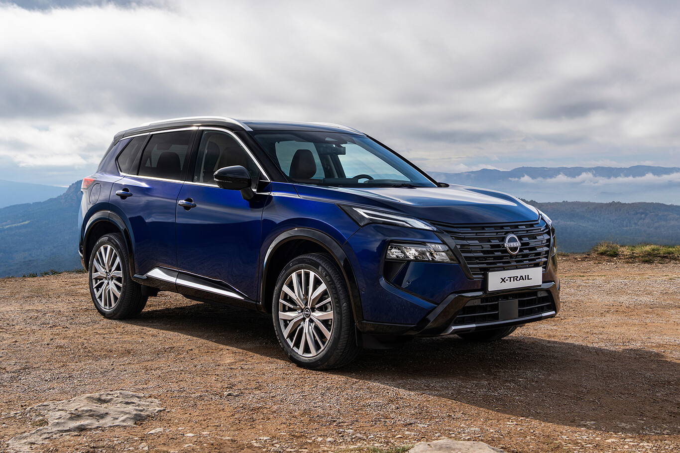 Nissan X-Trail 2026 bleu présenté de trois quarts avant dans un paysage montagneux
