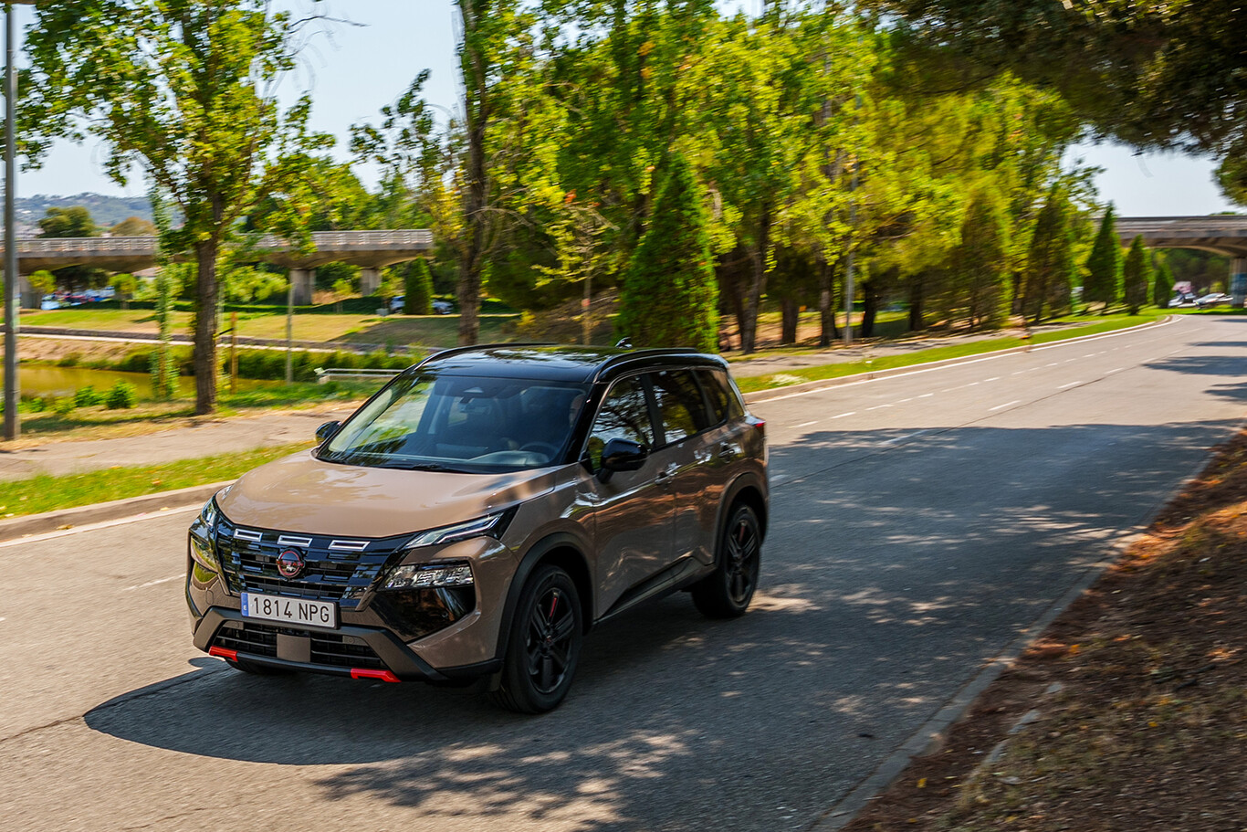 Nissan X-Trail beige roulant sur une route arborée en ville