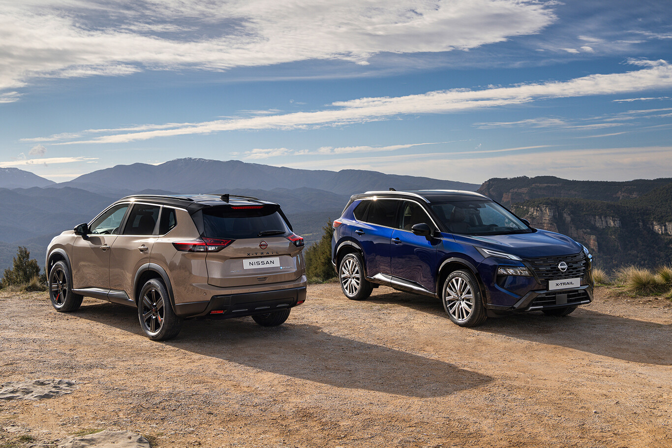 Deux Nissan X-Trail 2026 beige et bleu stationnés face aux montagnes