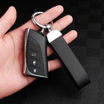 Main tenant une clé de voiture noire attachée à un porte-clés en cuir noir, avec anneau métallique argenté