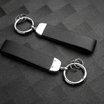 Deux porte-clés en cuir noir, dotés d’anneaux métalliques argentés, posés sur une surface texturée gris foncé