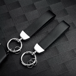 Deux porte-clés en cuir noir avec attache métallique argentée, posés sur une surface texturée noire.