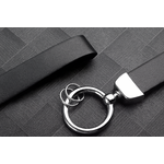 Gros plan sur un porte-clés en cuir noir, doté d’un anneau métallique argenté posé sur une surface texturée sombre