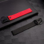 Deux porte-clés en tissu noir et rouge avec mousqueton, sans logo, posés sur fond sombre