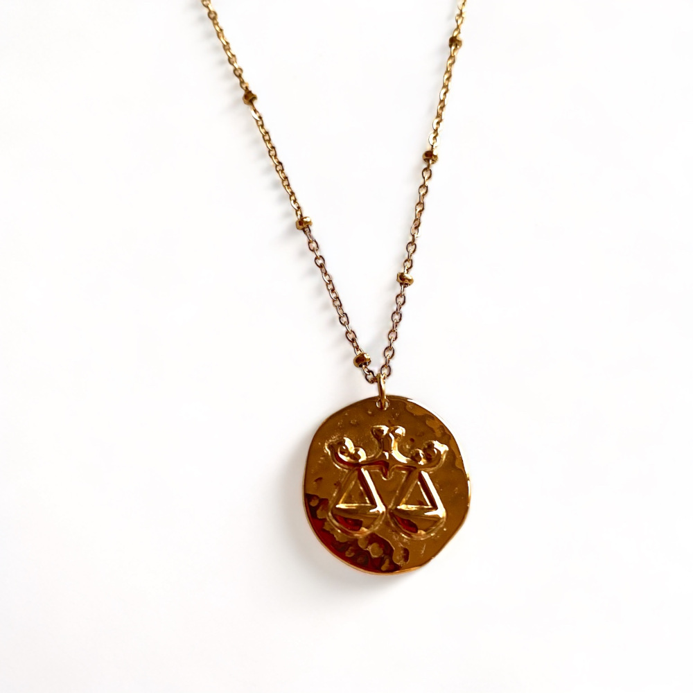 collier avec medaille frappee avec une balance symbolisant le signe astrologique expose fond blanc