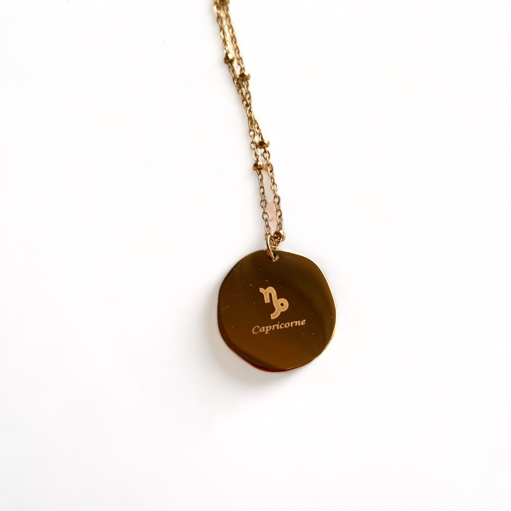 collier medaillon lisse au dos avec le signe astrologique capricorne ecrit mis en valeur fond blanc