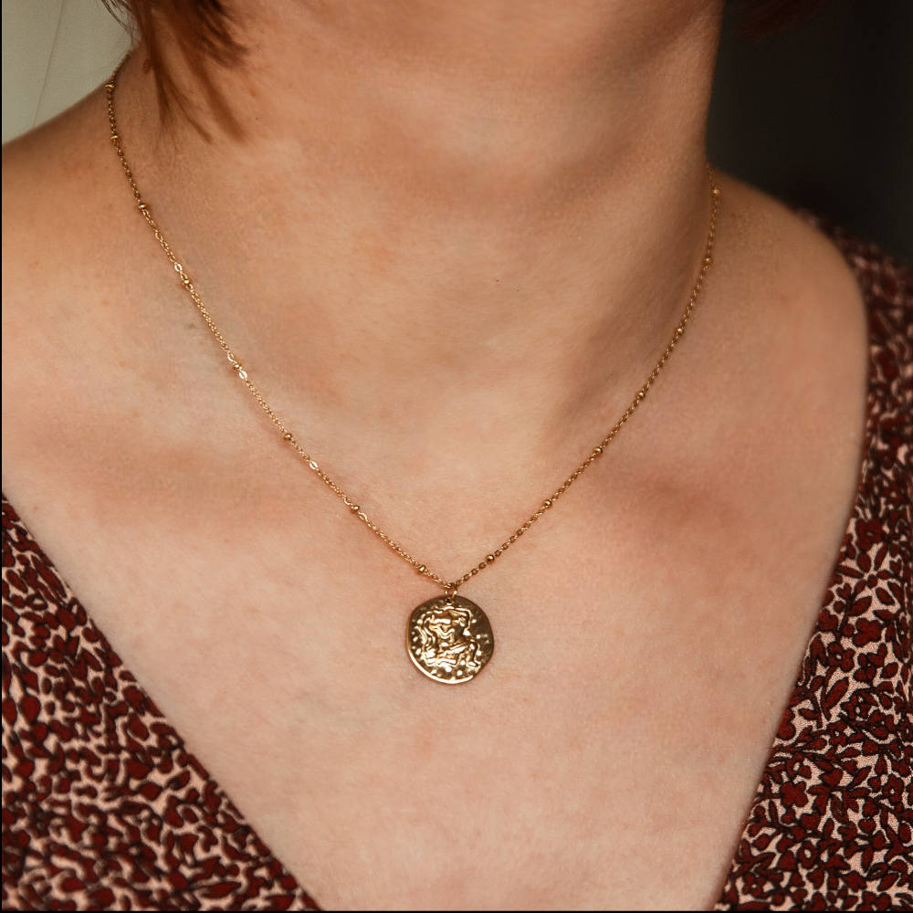 collier avec medaille en relief avec un motif symbolisant le signe astrologique verseau expose sur fond blanc