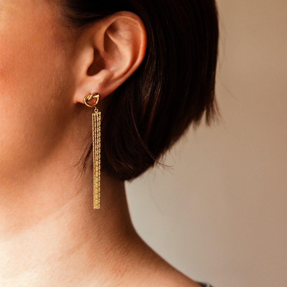 boucles d oreilles chaines pendantes dorees avec accroche forme anneau creux et motif noeud portees oreille gauche paloma