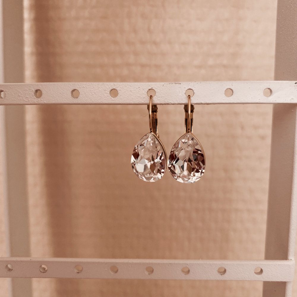 boucle oreille pendante cristal transparent forme goutte et monture dormeuse en acier inoxydable dore mise en valeur sur presentoir naelle