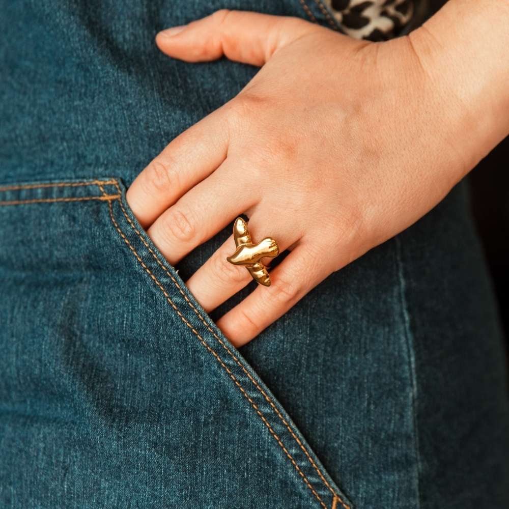 bague oiseau Luna dorée portée a la main avec jean bleu en arrière plan