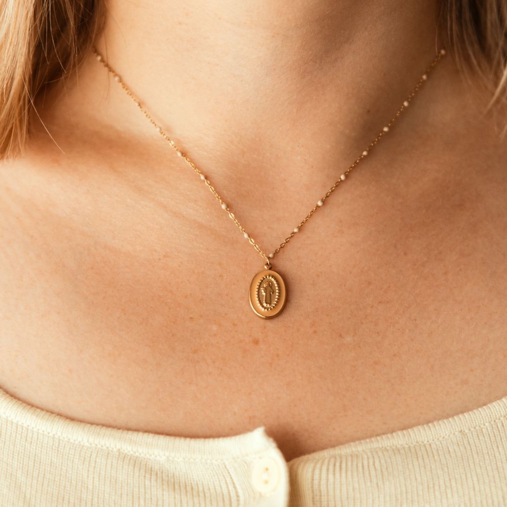 collier Vierge Marie doré porté autour du cou avec médaillon ovale et petites perles émaillées beige