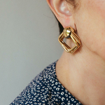 boucles d oreilles en forme de carre volumineuses et dorees portees oreille droite romane