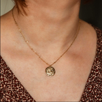 collier avec medaille en relief avec un motif symbolisant le signe astrologique verseau expose sur fond blanc