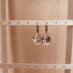 boucle oreille pendante cristal transparent forme goutte et monture dormeuse en acier inoxydable dore mise en valeur sur presentoir naelle