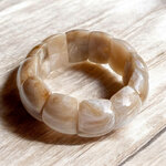 bracelet avec des grosses perles de couleur beige marbre style manchette elna expose sur fond en bois clair