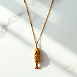 collier poisson en acier dore avec pendentif martele et lisse au verso chaine alternee mis en valeur sur fond en marbre rosalie